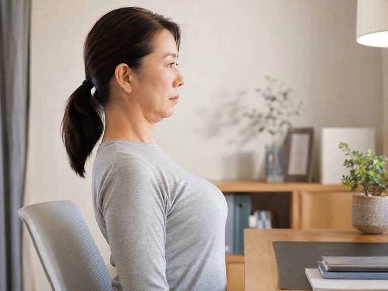 책상에 앉아 턱 당기기 목 운동을 하는 중년 여성